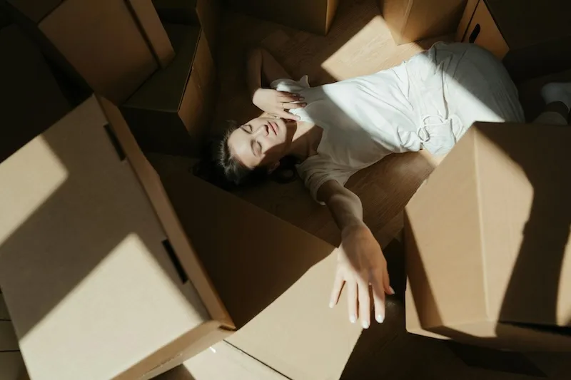 Une personne allongée au sol au milieu de cartons de déménagement ouverts