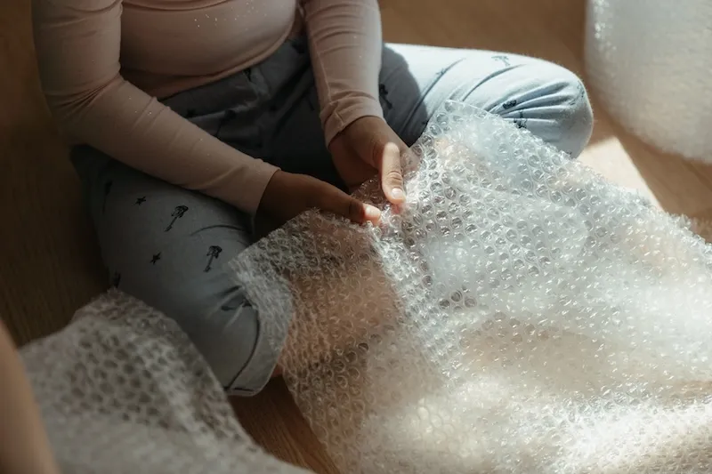 Une personne assise au sol déroule du papier bulle pour emballer ses affaires