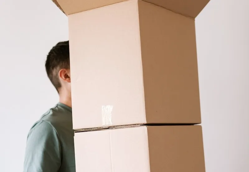 Un homme porte une haute pile de cartons de déménagement fermés